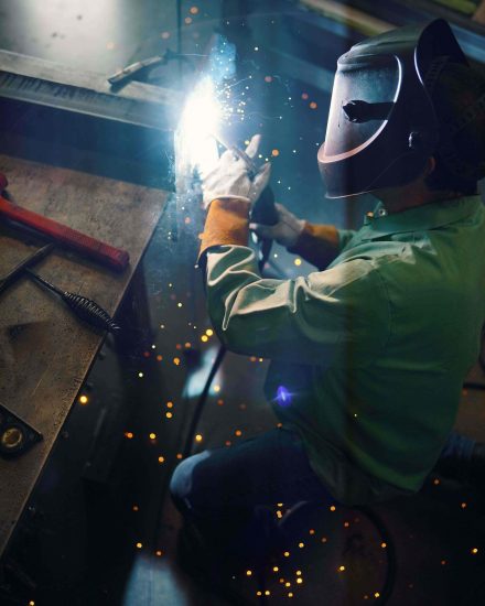 Tradesperson welding a metal workpiece with protective gear, controlled flame for clean cuts.